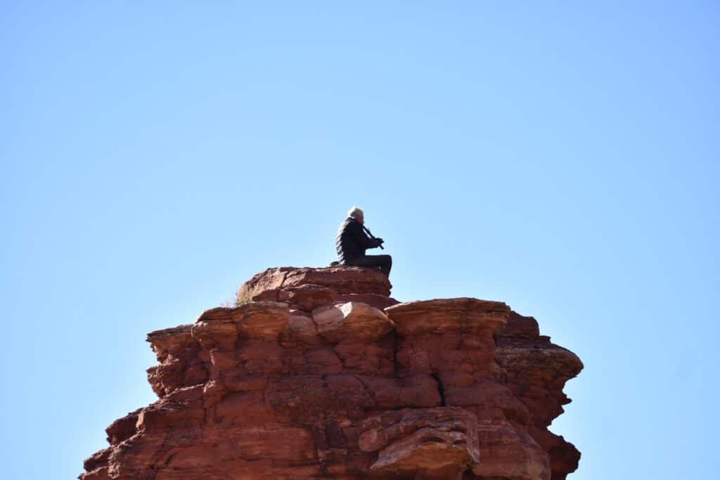 photo of a man on top of a rock formation playing a flute