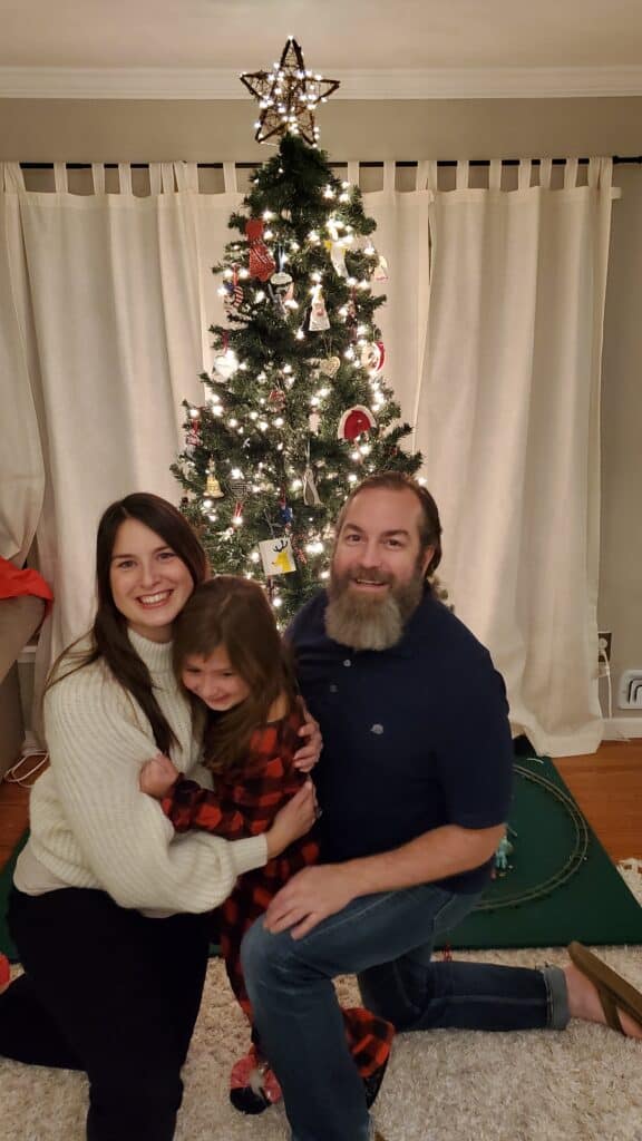 photo of Lee Ann with her husband and daughter in front of their Christmas tree