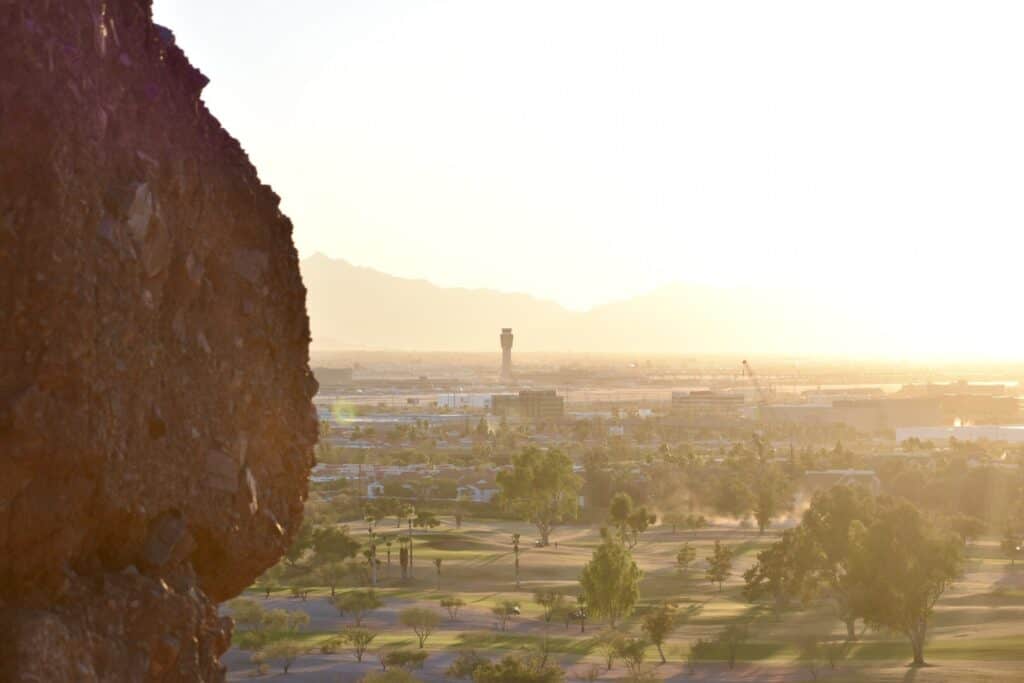 photo of a vertical rock in the foreground on the left side of the frame, bright sun whiting out the upper right of the frame, and the air traffic control tower for the airport in between